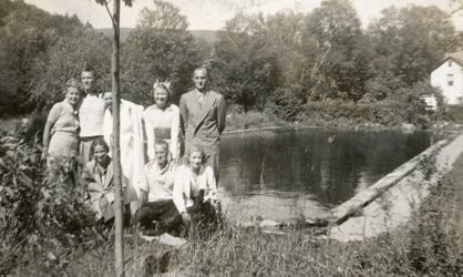 Kvinner og menn samlet til fotografering. I bakgrunnen et basseng og et hus