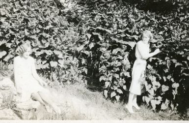 To unge kvinner, en sittende i gresset, en stående