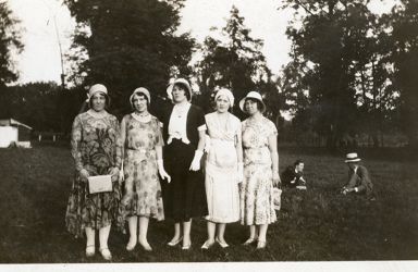 Fem kvinner med kjole og hatt. Kristine Gullestad midt i bildet og Ingeborg Gullestad i lys kjole ved siden av